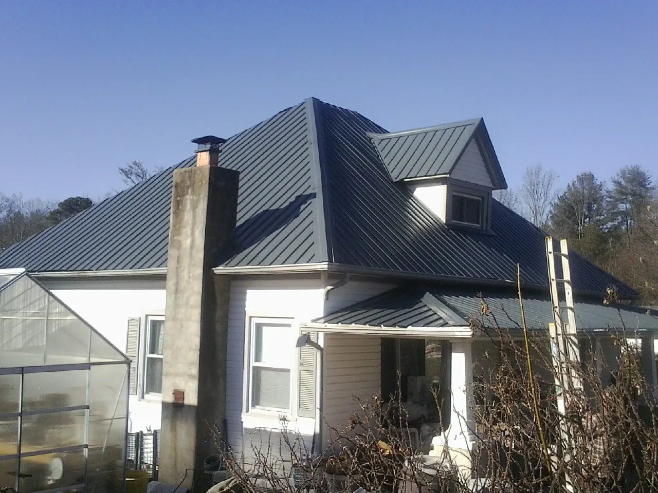 Dark blue standing seam metal roof on a white farmhouse with dormer — Slate & Tile Roof Repair by Roofing Brothers in Bozman