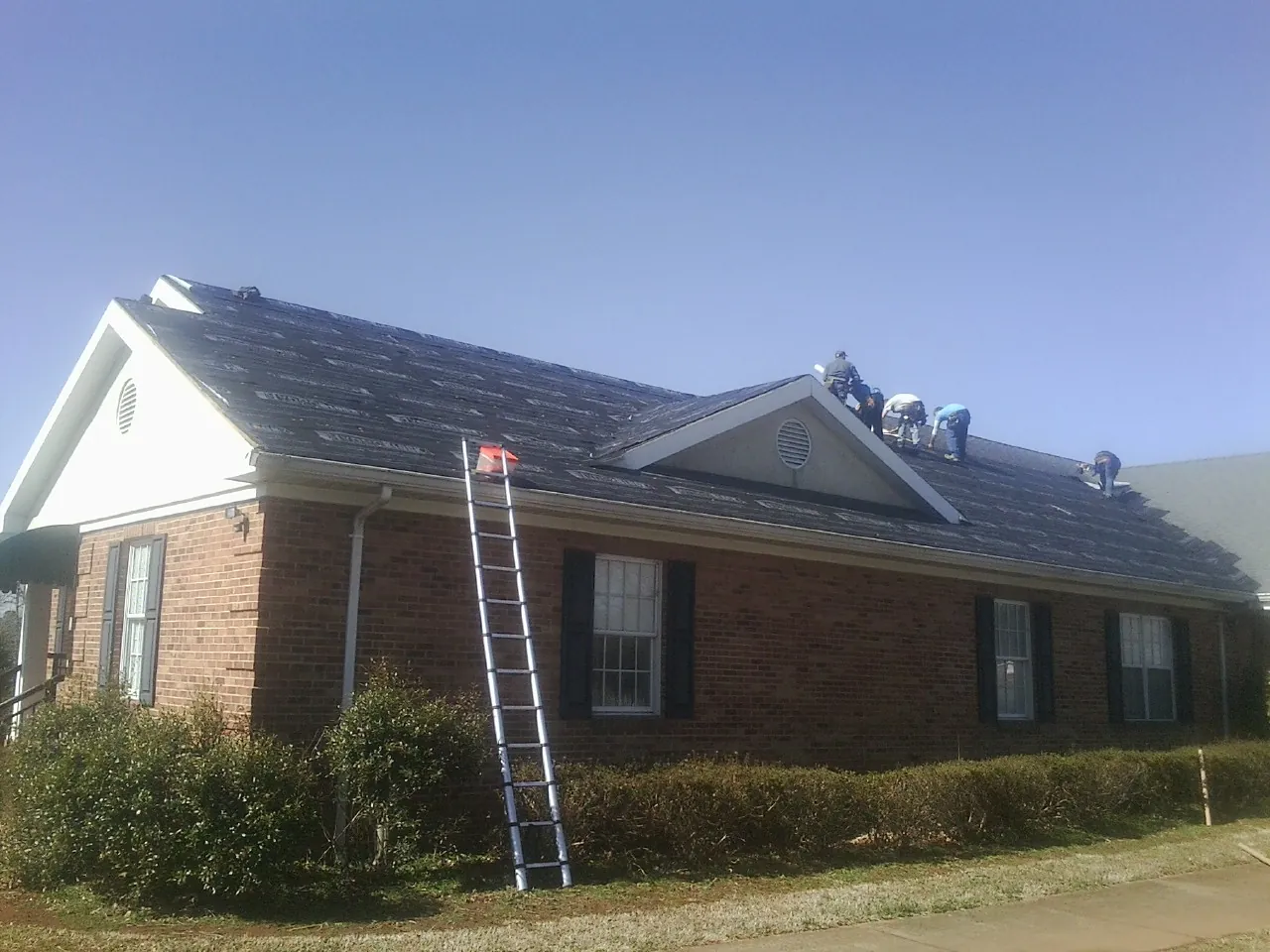 Crew tearing shingles off a brick ranch roof with a ladder set — Metal Roof Repair work by our crew in Bozman