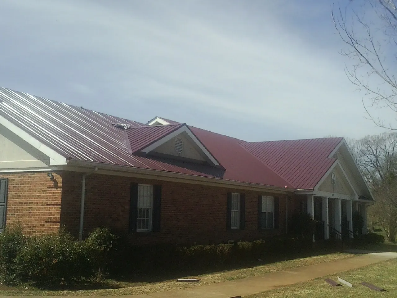 Red metal roof with gabled entries on a long brick building, from a Hail Damage Roof Repair job in Bozman