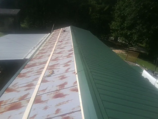 Old rusted panels beside newly installed green metal roofing — Wind Damage Roof Repair by Roofing Brothers in Bozman