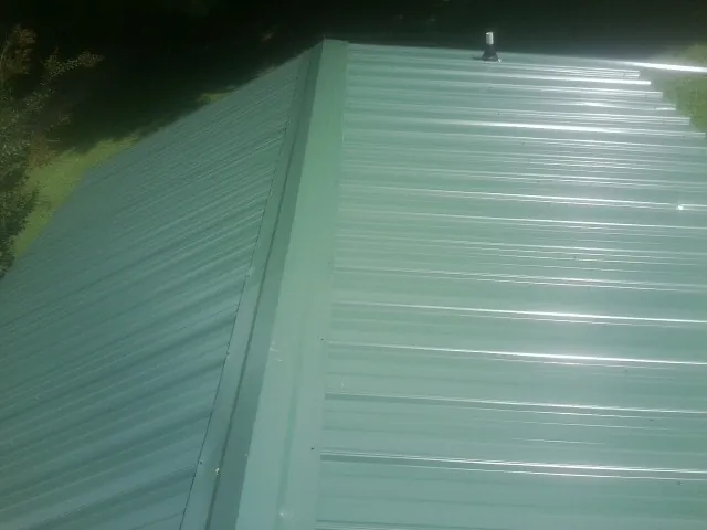 New green metal panels meeting at the ridge of a roof — Flat Roof Repair work by our crew in Bozman
