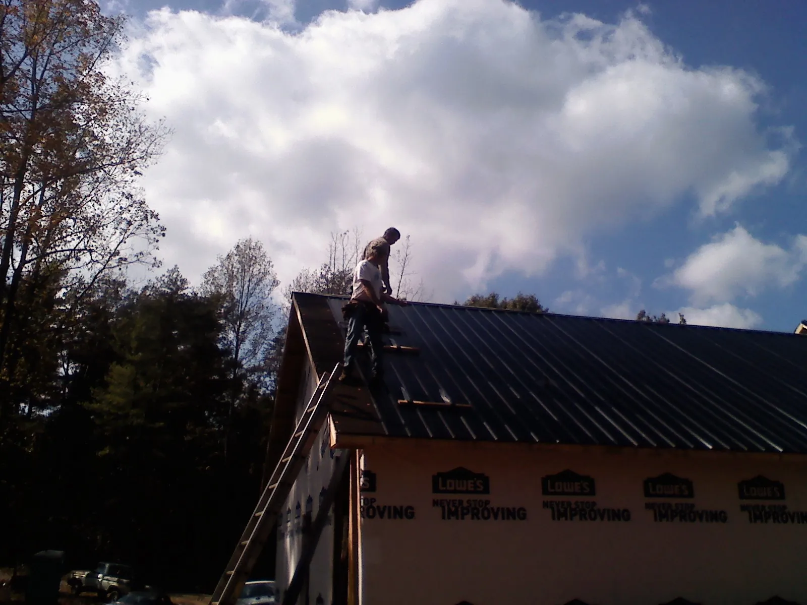 Roofer fastening dark metal panels high against a cloudy sky, from a Roof Inspection job in Bozman