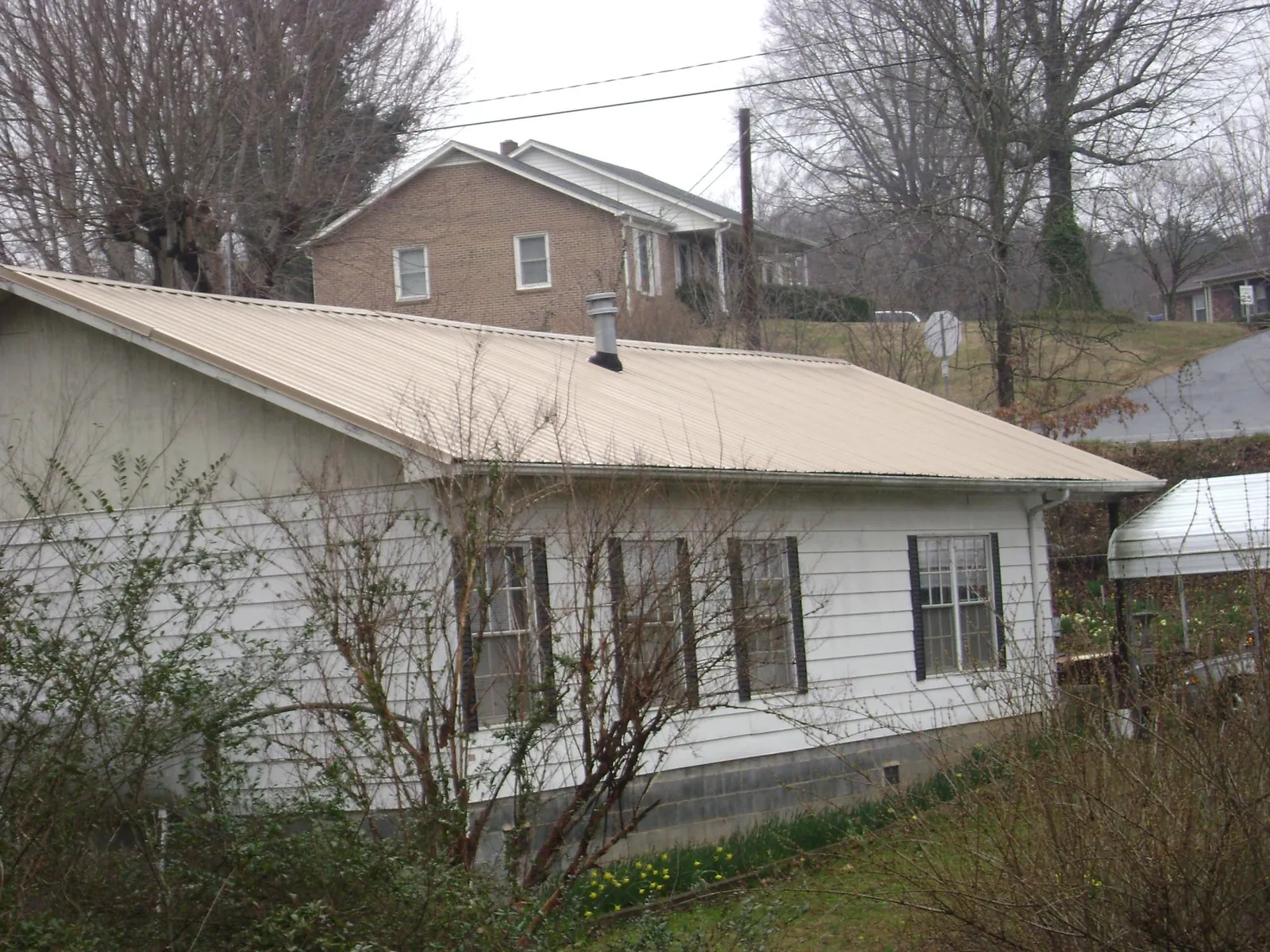 Tan metal roof on a white sided house set into a hillside — Commercial Roofing by Roofing Brothers in Bozman