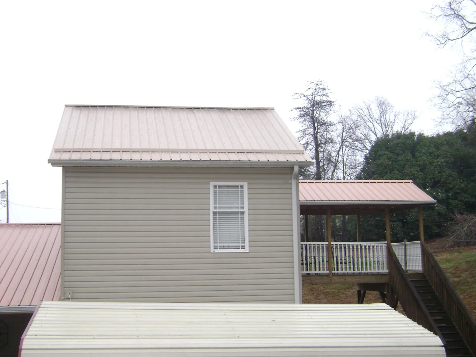 Tan metal roofs on a two story addition and attached porch, from a Roof Replacement job in Bozman